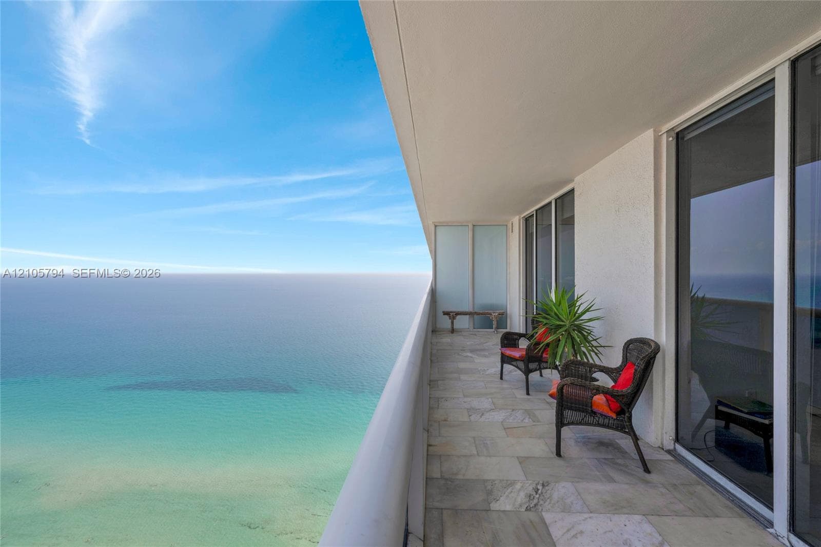 Covered balcony featuring stone-tile flooring, glass-panel privacy partition, and floor-to-ceiling sliding glass door access