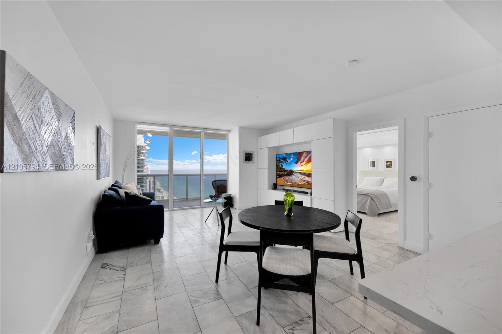 Floor-to-ceiling glass sliding doors, stone-finish tile flooring, built-in white wall cabinetry, and ocean backdrop