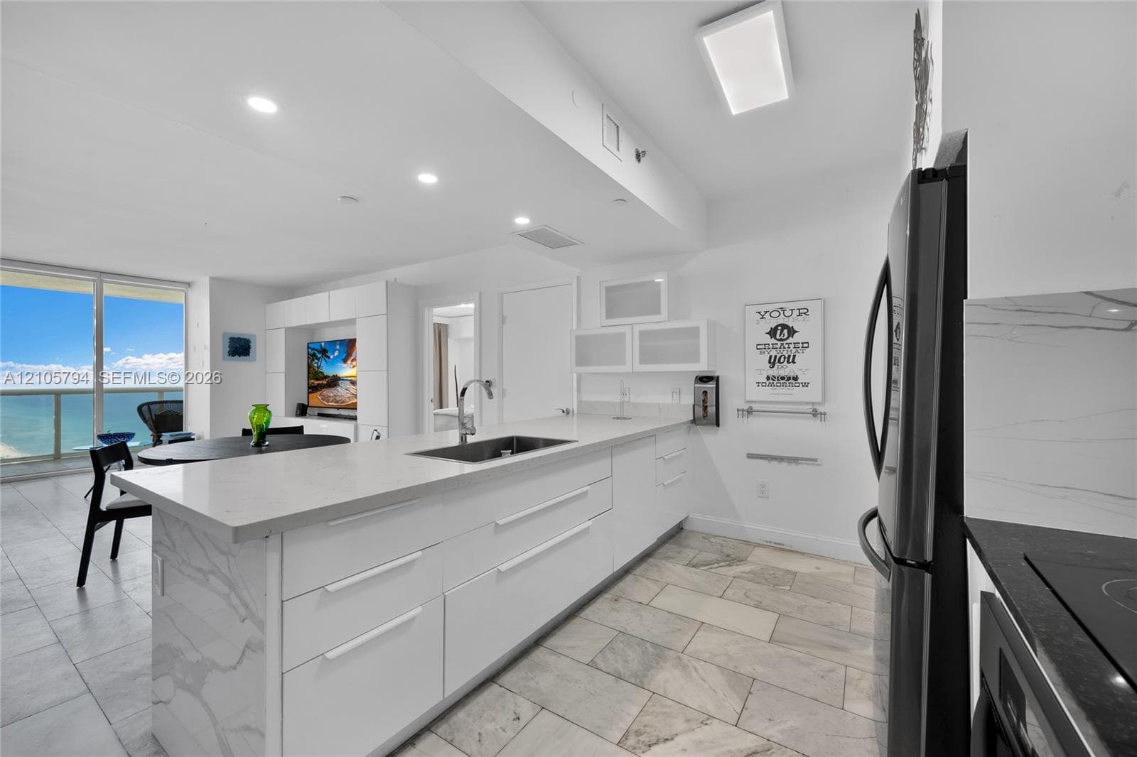 Kitchen featuring white cabinetry with stone-surface countertops, waterfall-edge island, undermount stainless steel sink, tile flooring, and integrated lighting