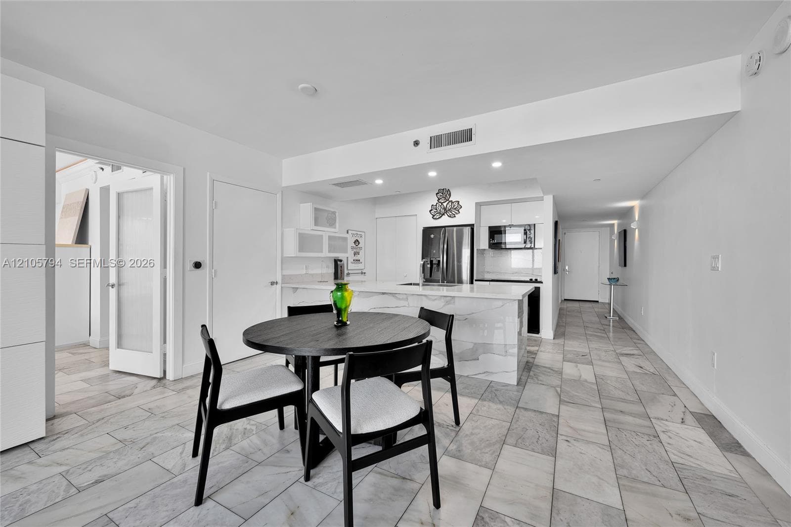 Kitchen featuring a waterfall-edge stone island, high-gloss cabinetry, stainless steel appliances, recessed lighting, and stone flooring