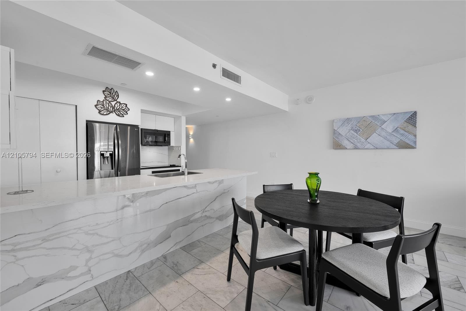 Kitchen featuring a waterfall-edge island with stone-finish countertop, stainless steel refrigerator, built-in microwave, and stone-finish tile flooring