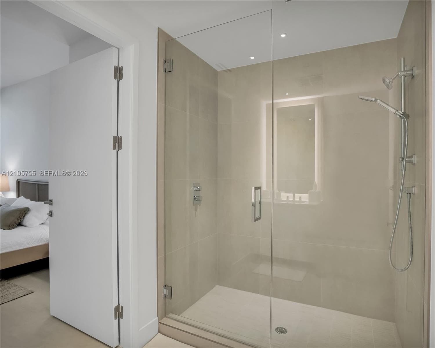 Walk-in shower featuring a frameless glass door, large-format tile surround, chrome hand-held shower fixture, and recessed lighting