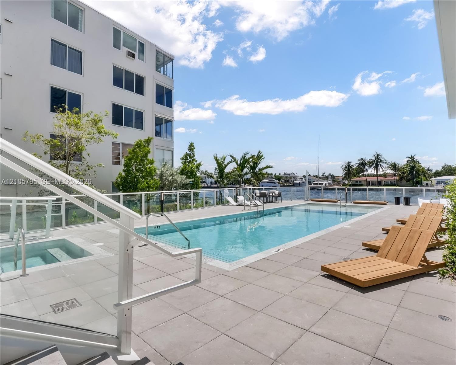 Swimming pool and spa area featuring large-format tile decking, glass perimeter railing, and waterfront orientation