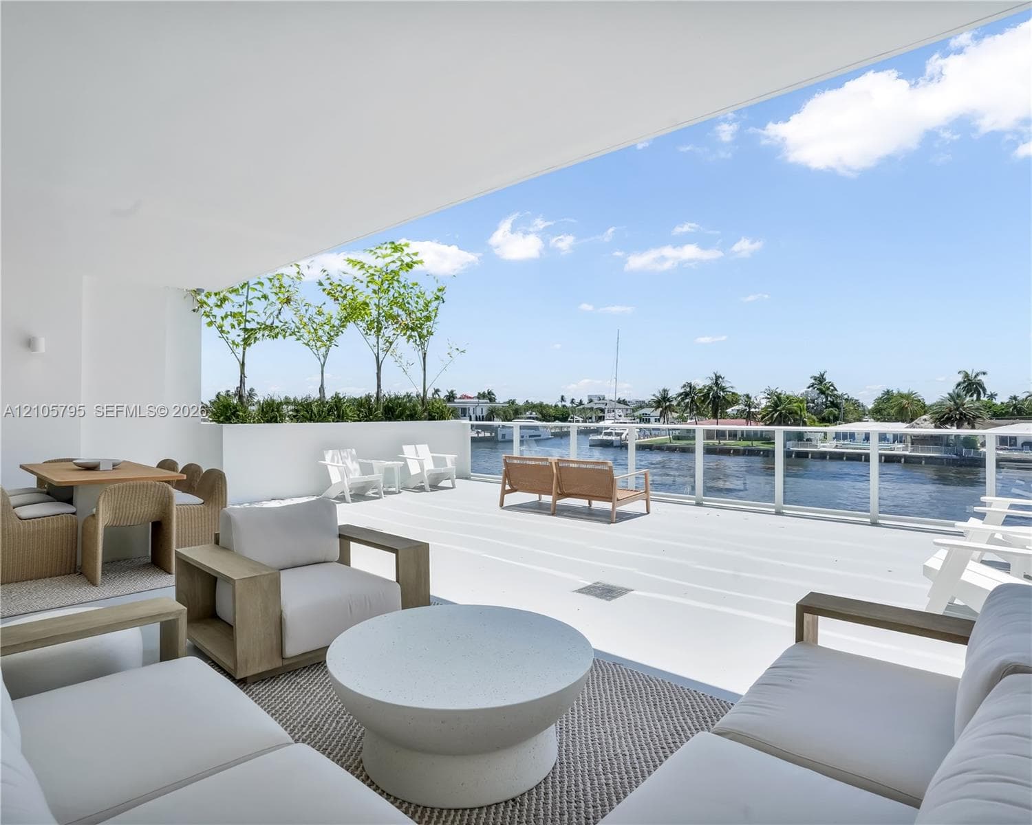 Expansive covered balcony featuring white decking, a minimalist white perimeter wall, and a full-length glass railing overlooking the waterway