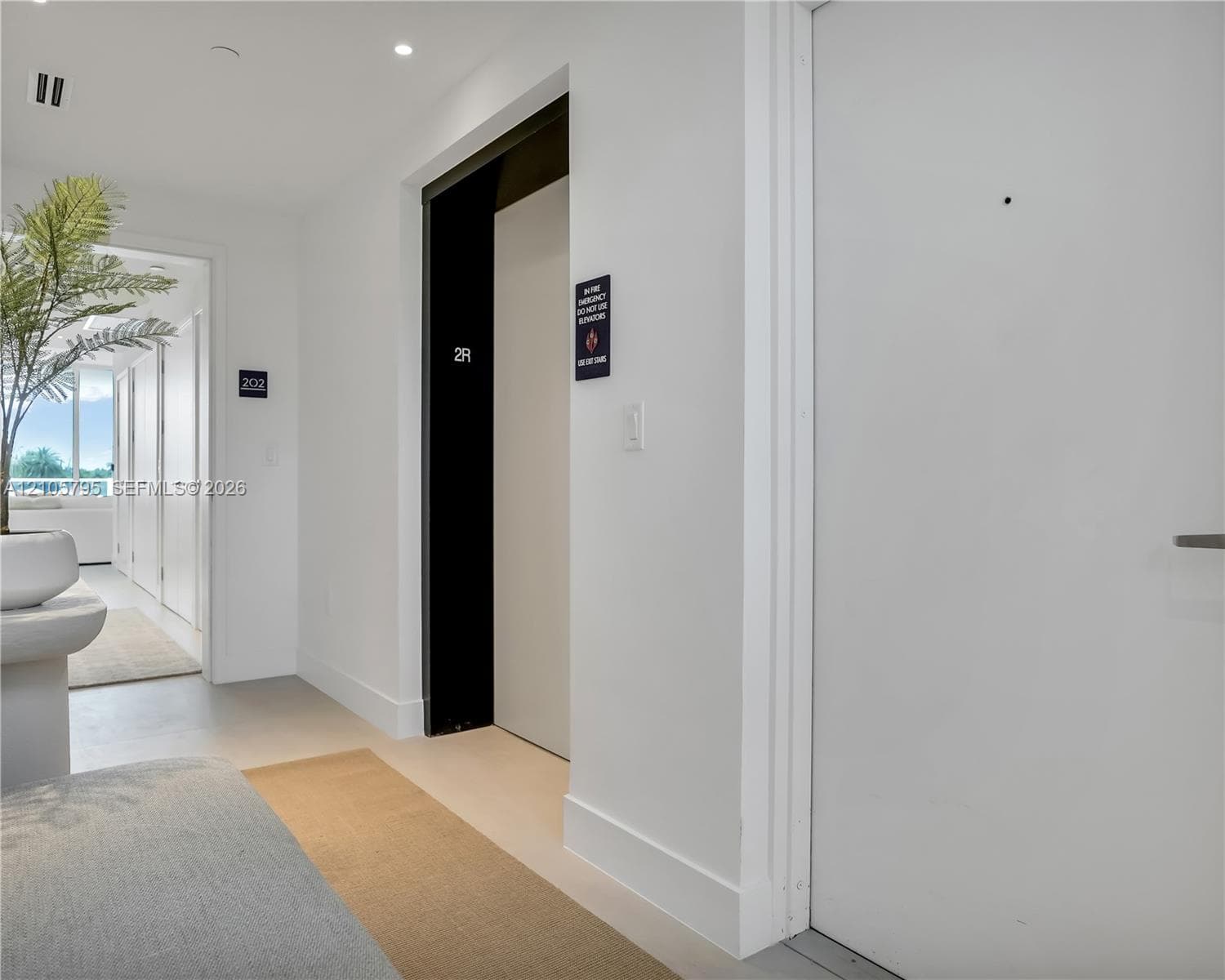 Hallway featuring smooth white walls, recessed ceiling lighting, light-toned flooring, and a dedicated elevator access point