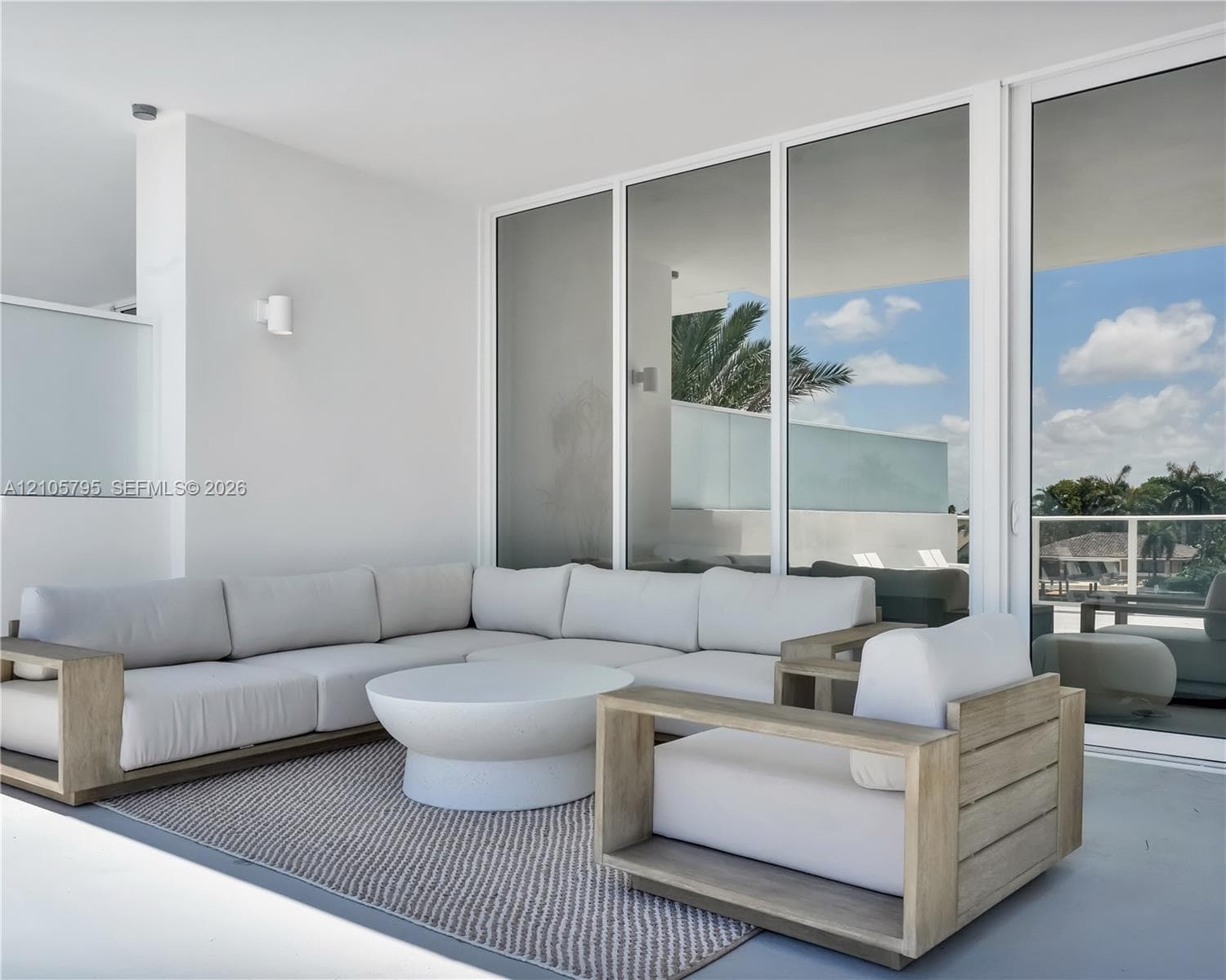 Covered patio featuring white-frame floor-to-ceiling glass sliding doors, smooth concrete flooring, and minimalist wall-mounted light fixtures