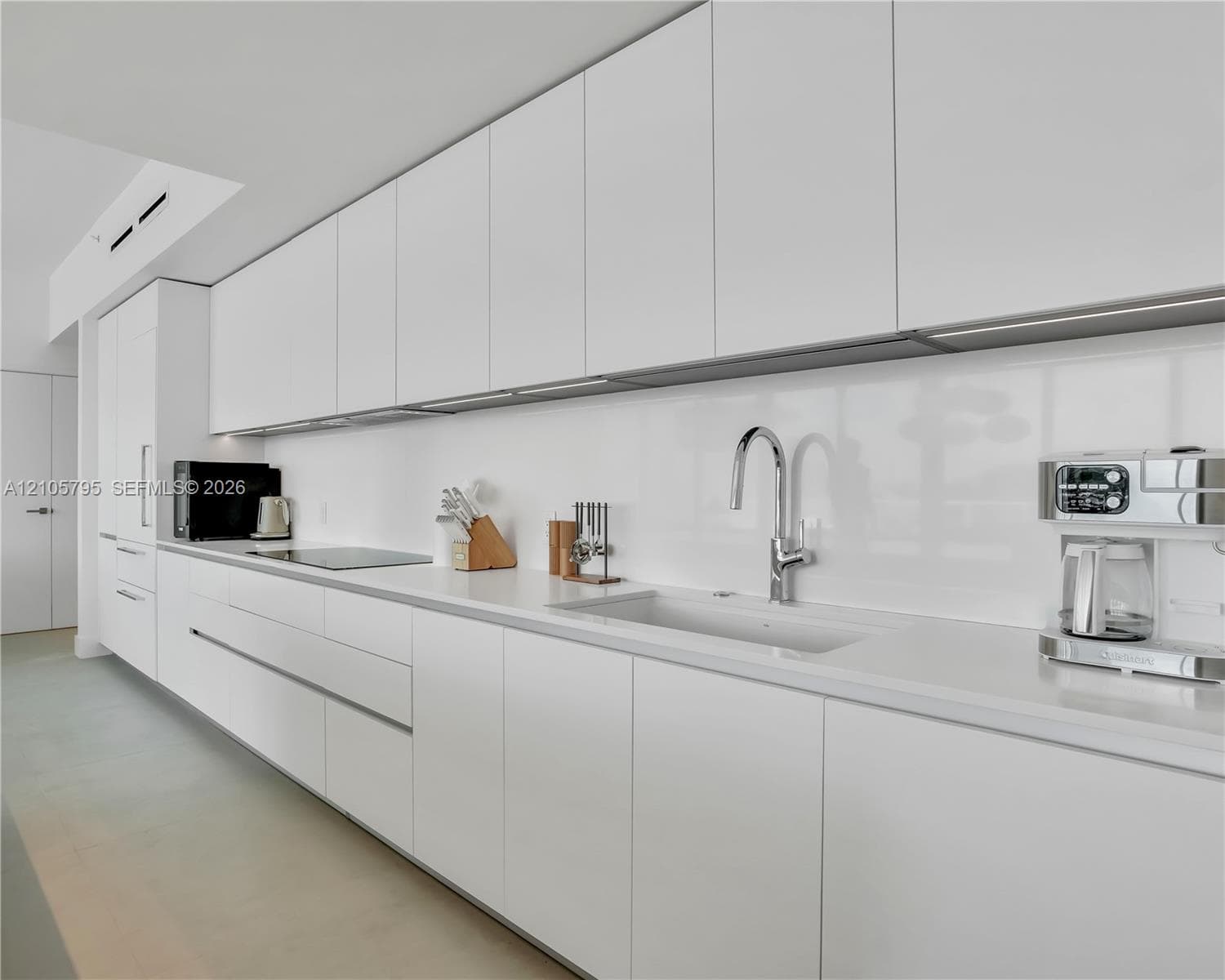 Minimalist kitchen featuring flat-panel cabinetry, solid-surface countertops, a seamless backsplash, an integrated induction cooktop, and a chrome gooseneck faucet