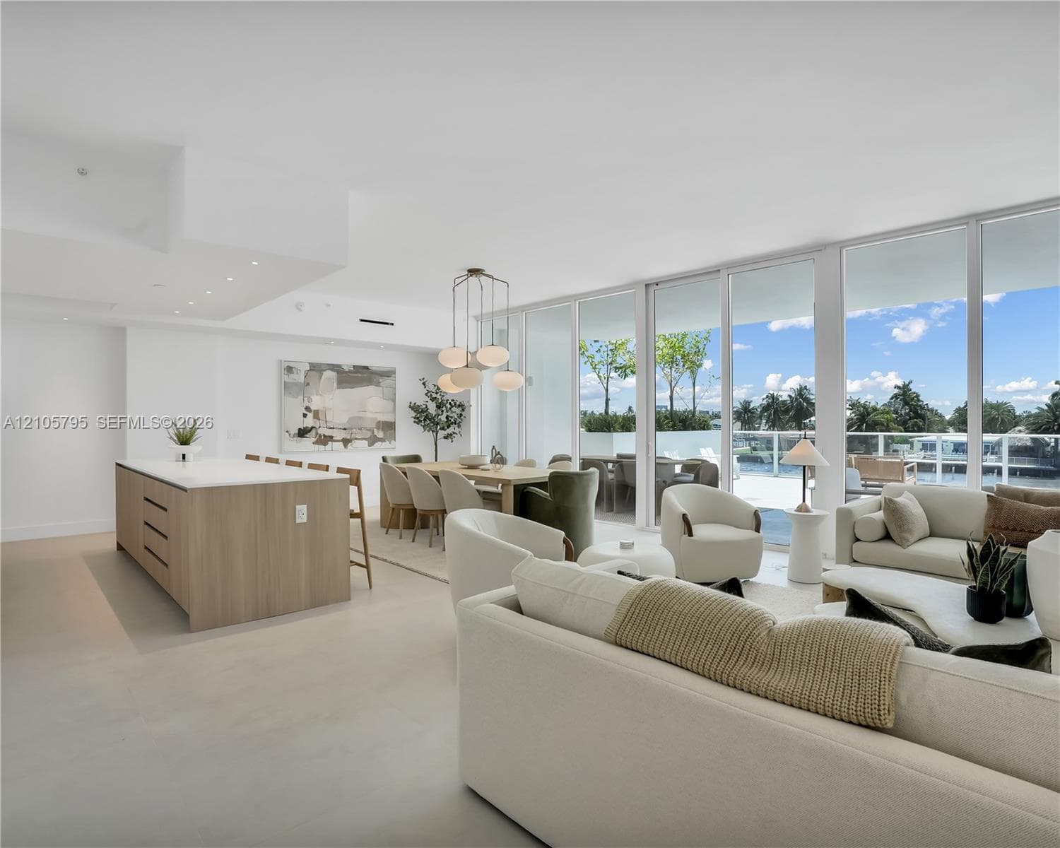Open-concept living space featuring floor-to-ceiling glass panels, a central kitchen island with a light-toned wood finish and solid surface countertop, polished flooring, and recessed lighting