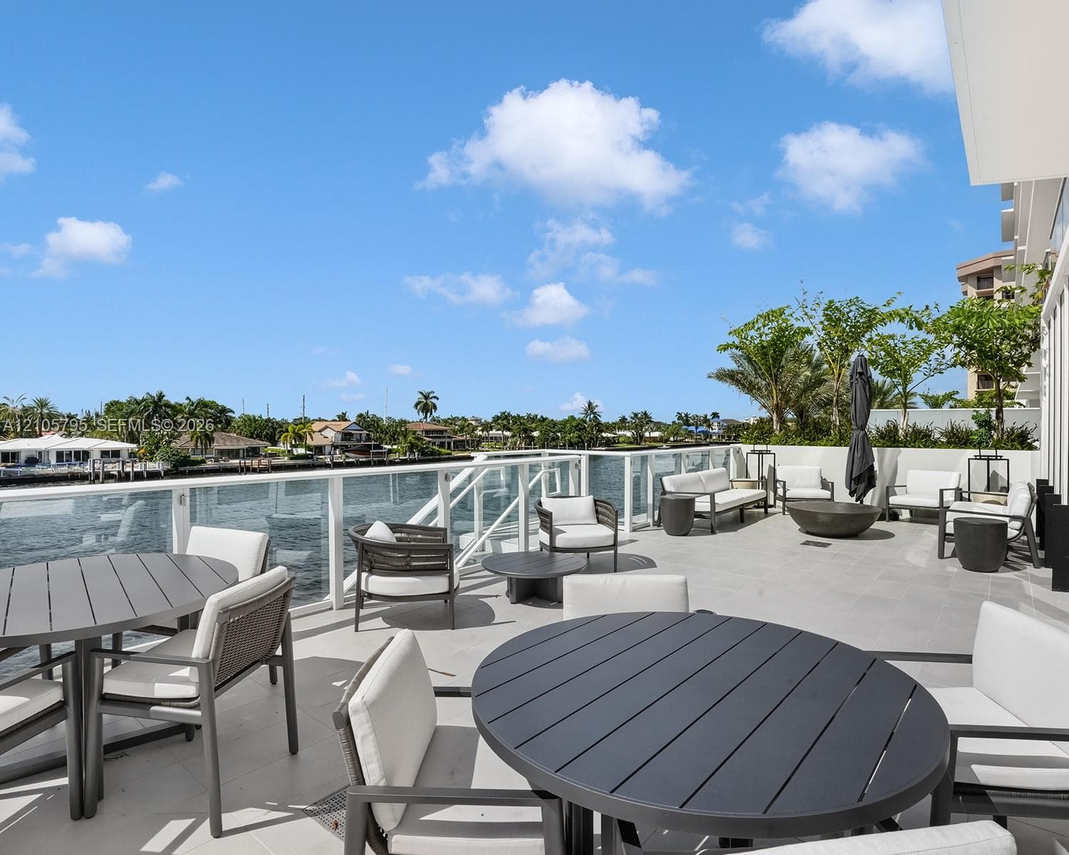 Expansive terrace featuring large-format tile flooring, a glass-panel railing system, and direct waterfront exposure