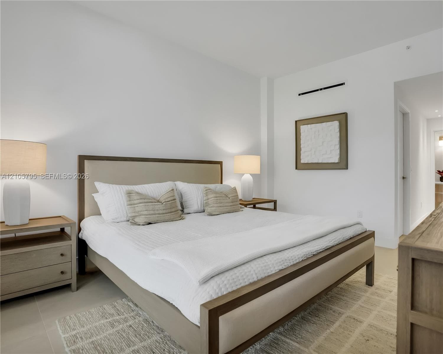 Neutral-toned interior featuring smooth wall surfaces, high ceilings, large-format tile flooring, and a wall-mounted climate control unit