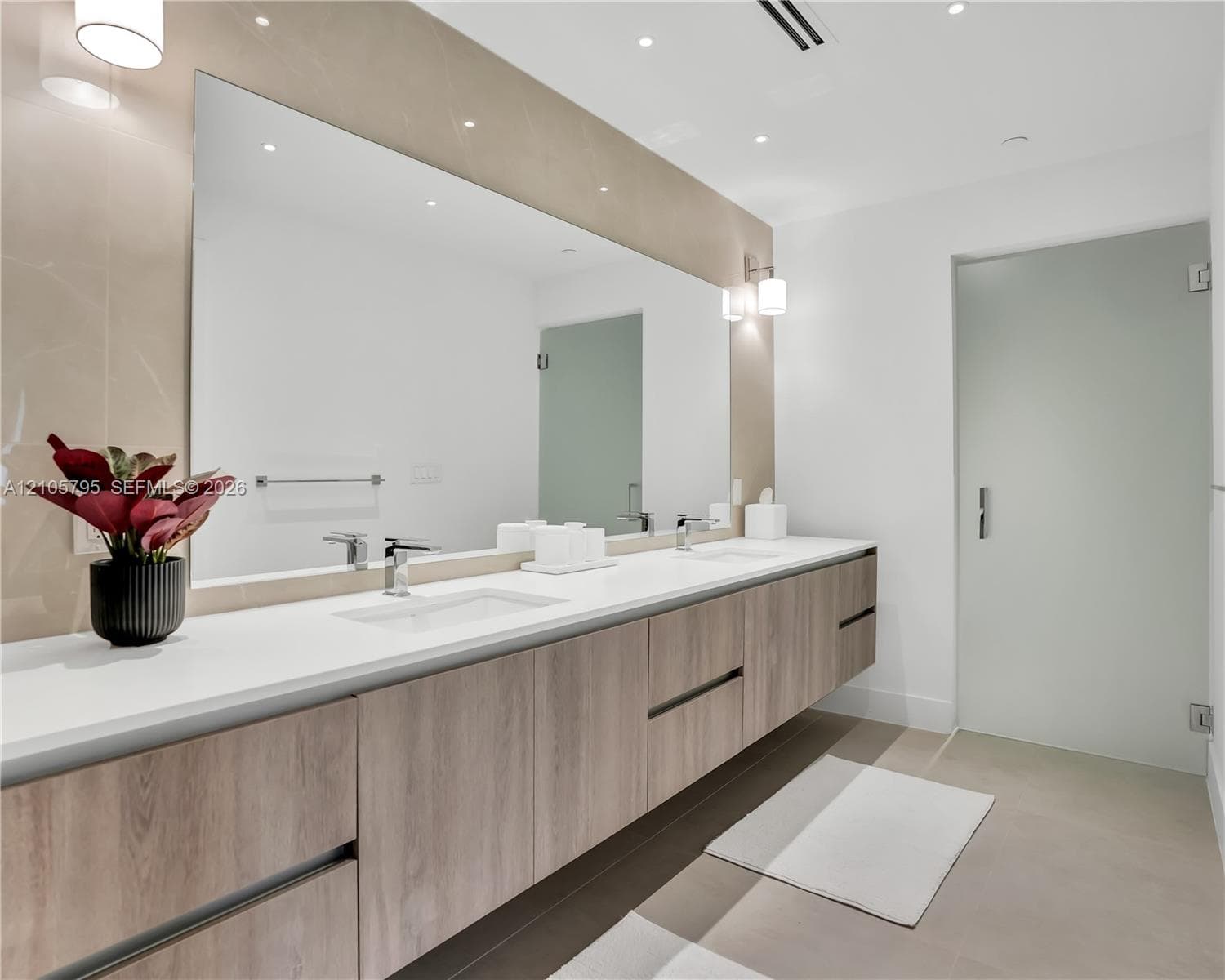 Floating wood-finish vanity with dual integrated rectangular sinks, expansive wall-to-wall mirror, quartz countertop, and frosted glass door