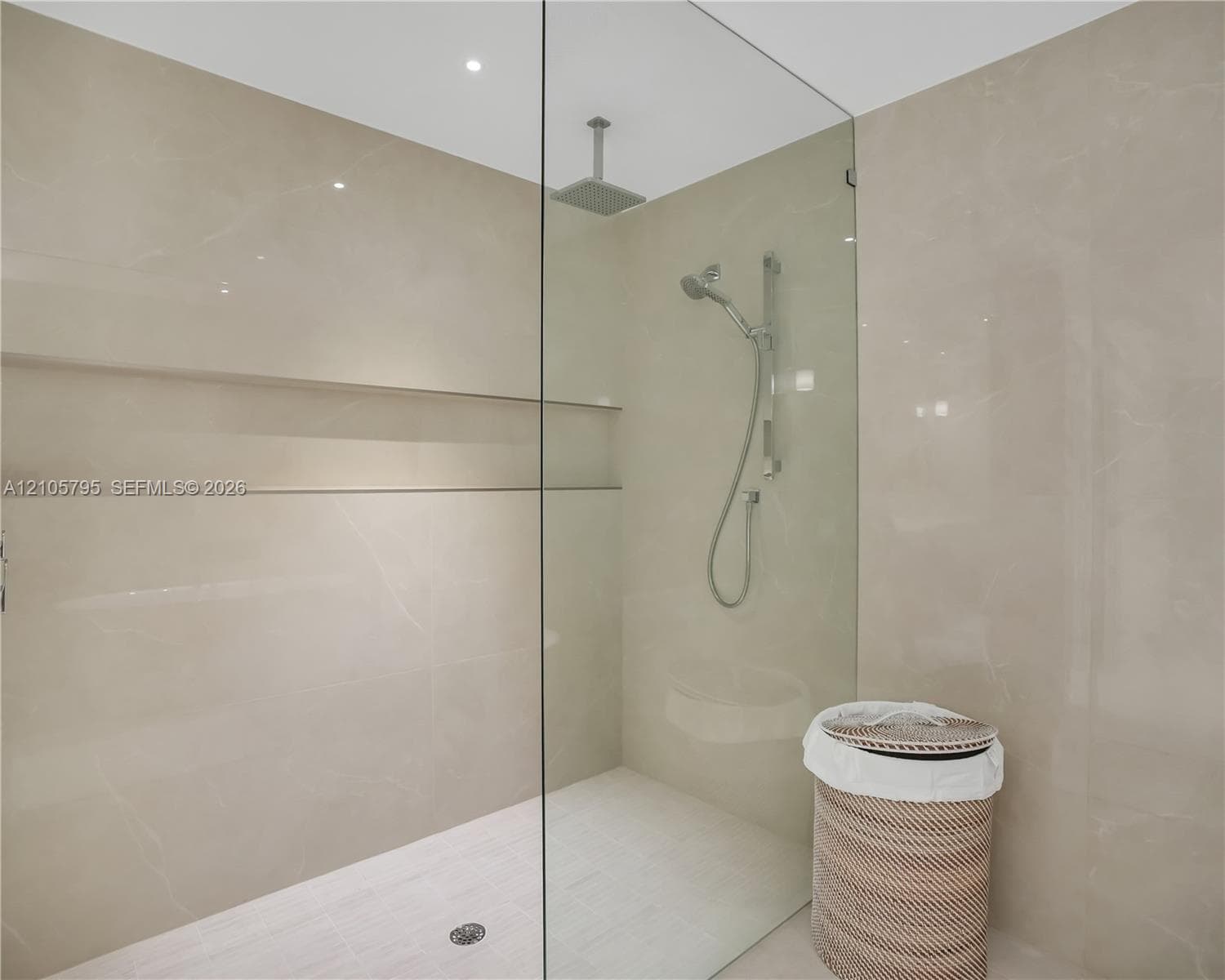 Walk-in shower featuring large-format stone-finish tile surround, integrated recessed shelving, a frameless glass enclosure, a ceiling-mounted rainfall showerhead, and a hand-held shower wand