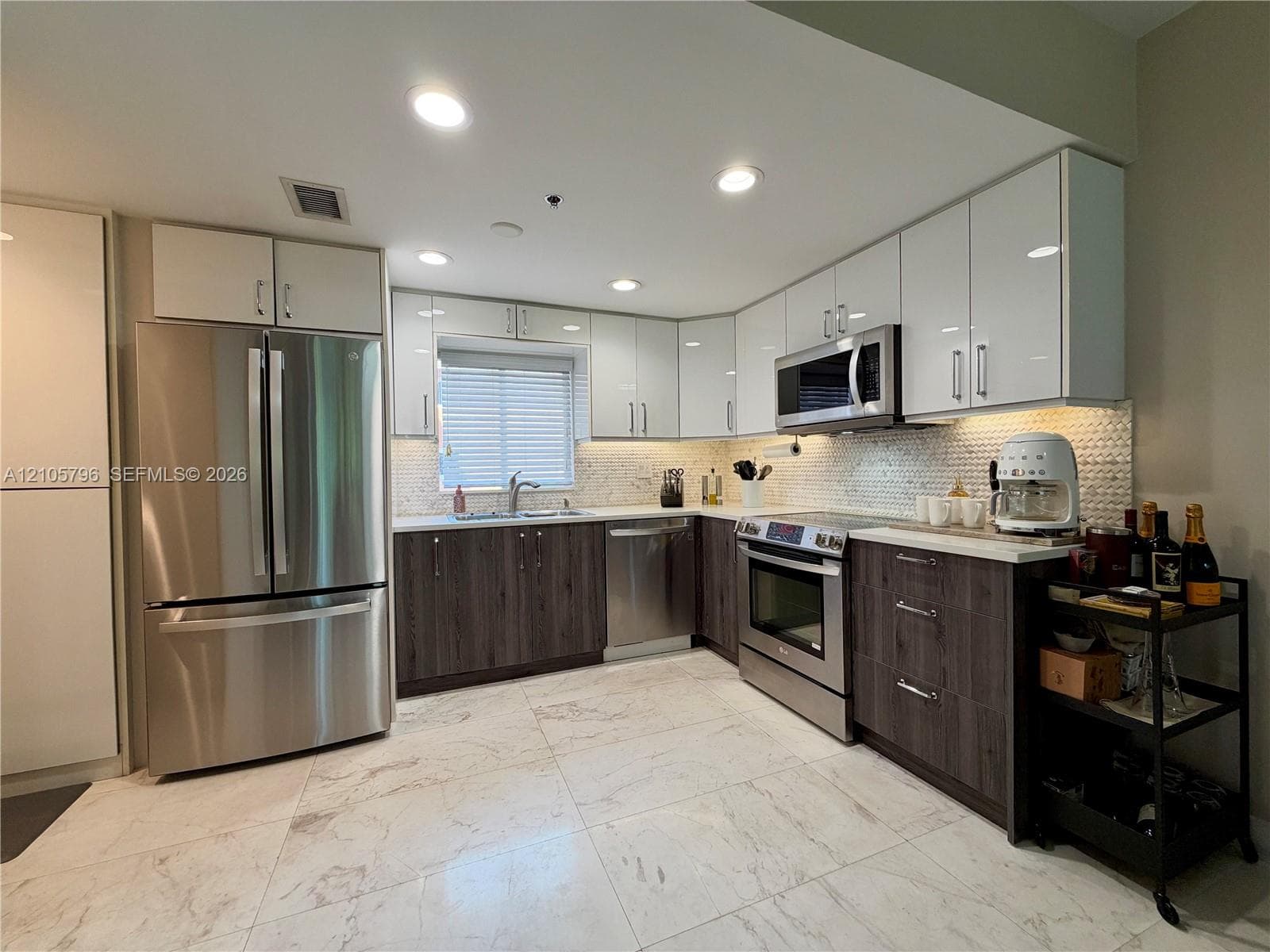 Kitchen featuring two-tone cabinetry with white upper and wood-finish lower cupboards, stone-patterned floor tiling, stainless steel appliances, and a mosaic tile backsplash