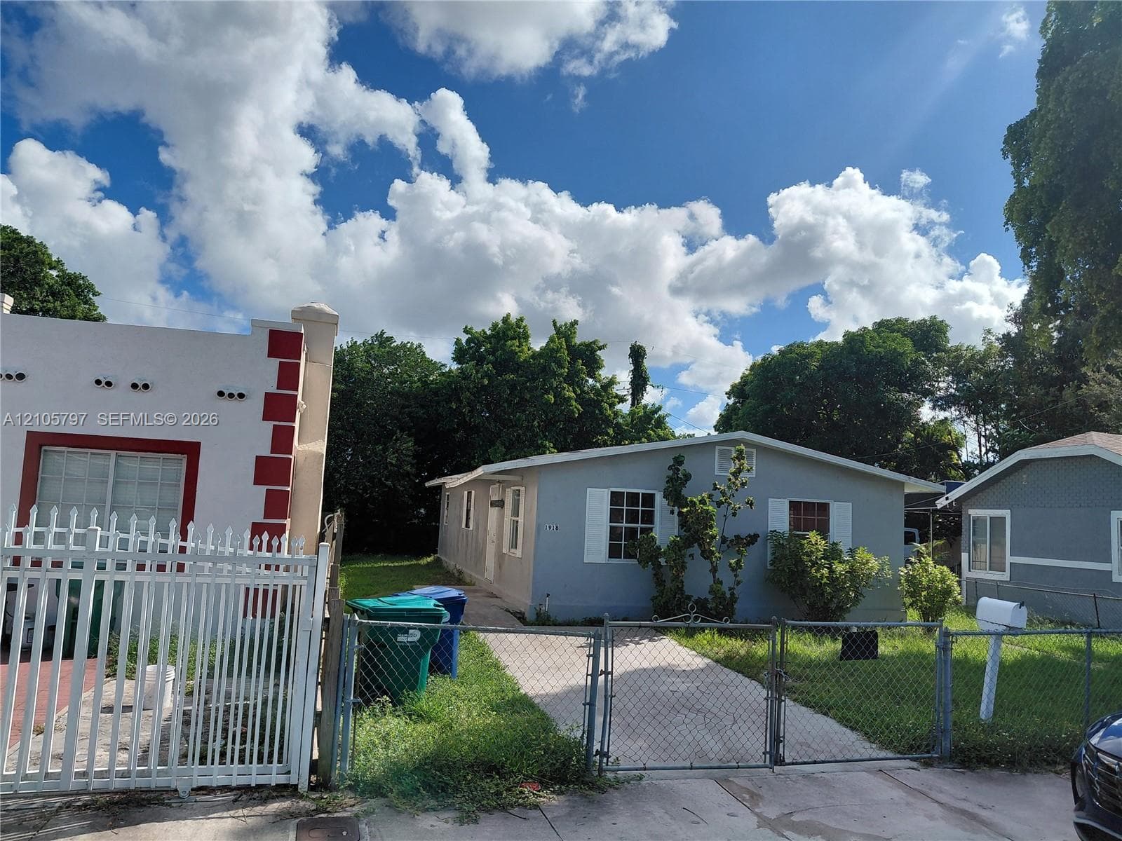 Single-story residence featuring light gray exterior siding, window shutters, and an attached concrete driveway secured by a chain-link fence