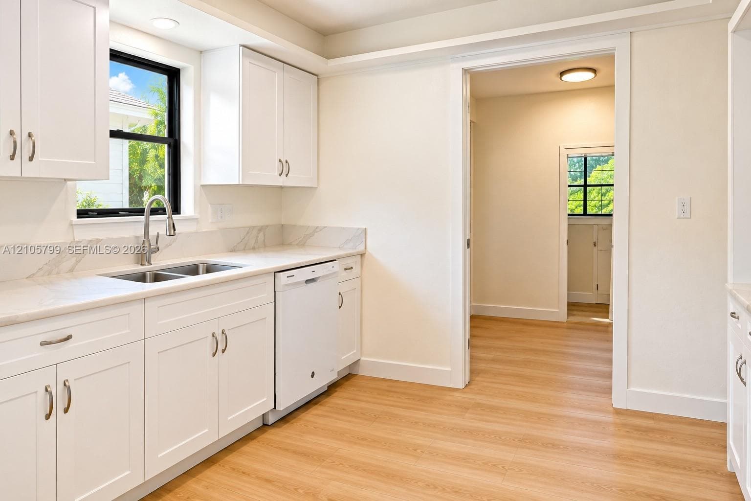Kitchen featuring white shaker-style cabinetry, stone-patterned backsplash, light-toned wood-finish flooring, undermount dual-basin sink, and recessed lighting