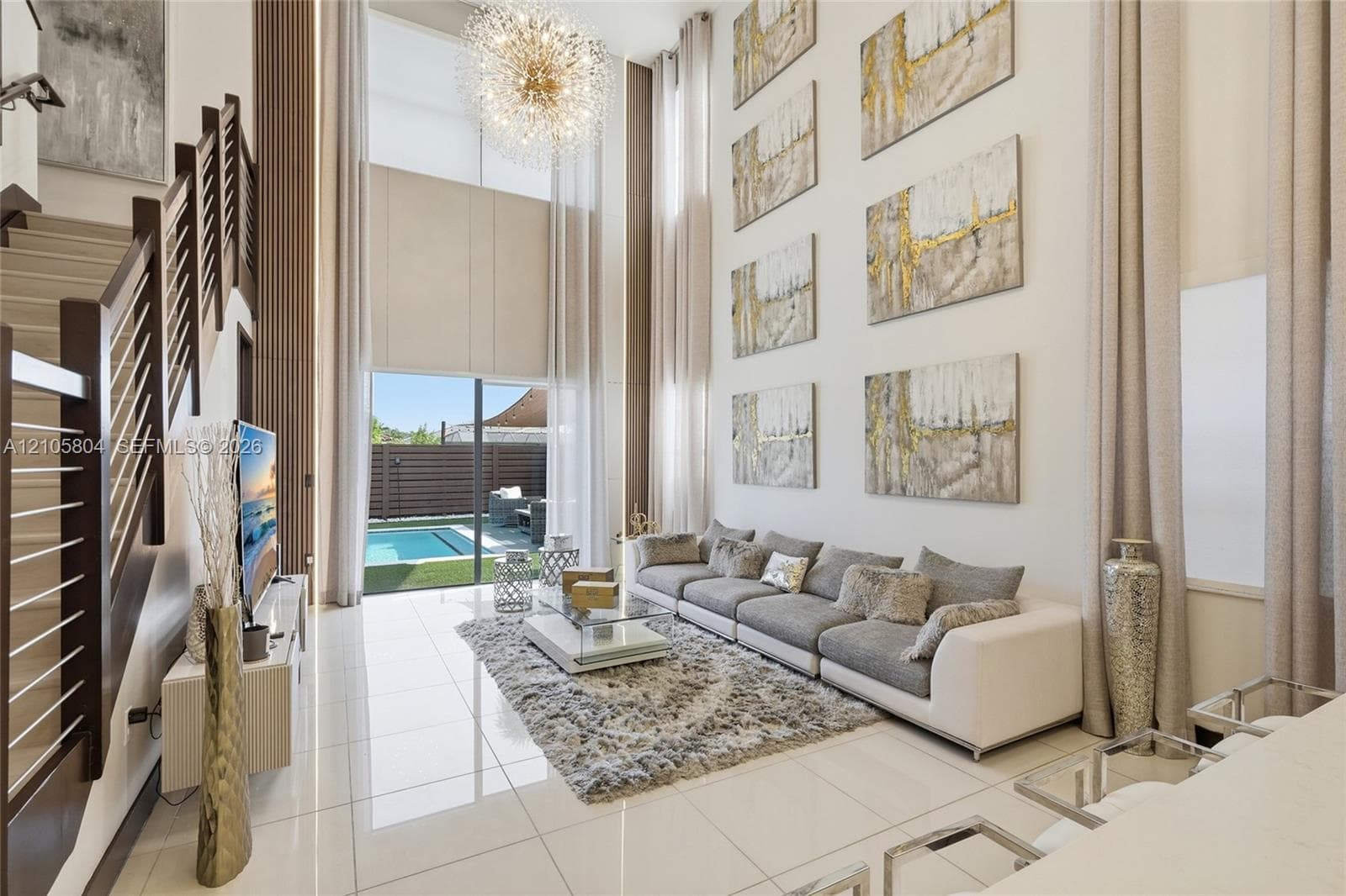 Double-height ceilings featuring floor-to-ceiling windows, polished tile flooring, a statement chandelier, and a staircase with a horizontal cable railing system