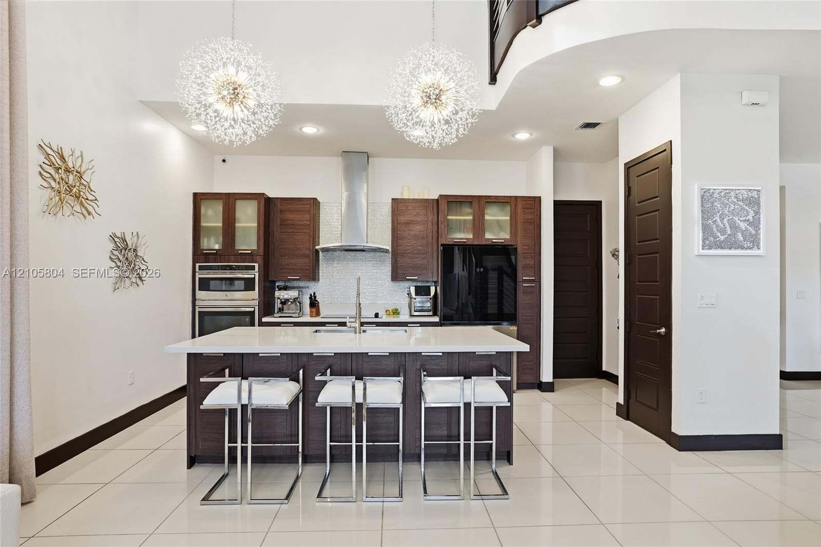 Kitchen featuring dark wood-finish cabinetry, a white stone island countertop, a stainless steel chimney-style range hood, recessed ceiling lighting, and two sphere-shaped pendant light fixtures