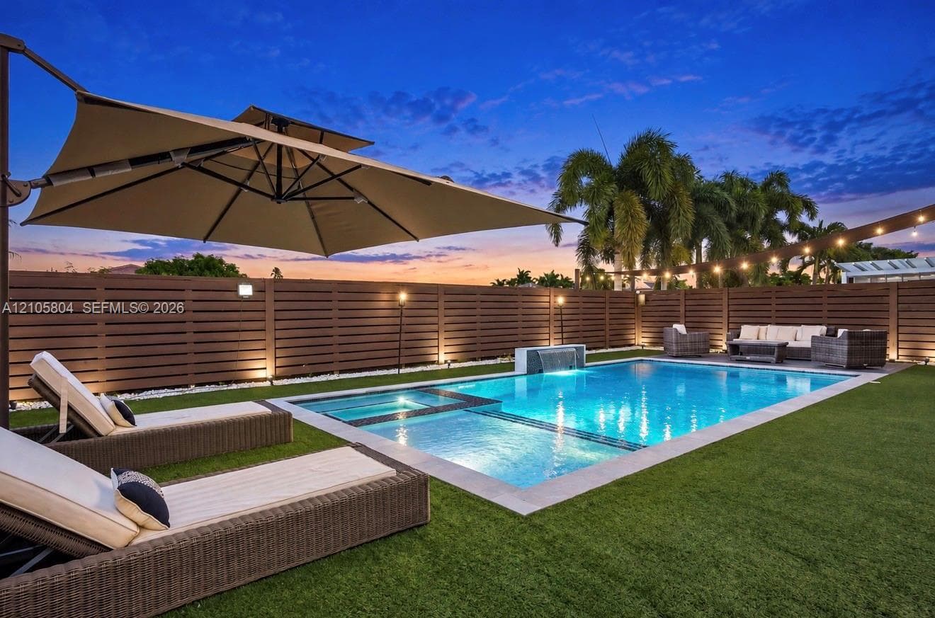 Backyard oasis featuring a swimming pool with integrated spa and water feature, surrounding synthetic turf, and perimeter horizontal privacy fencing