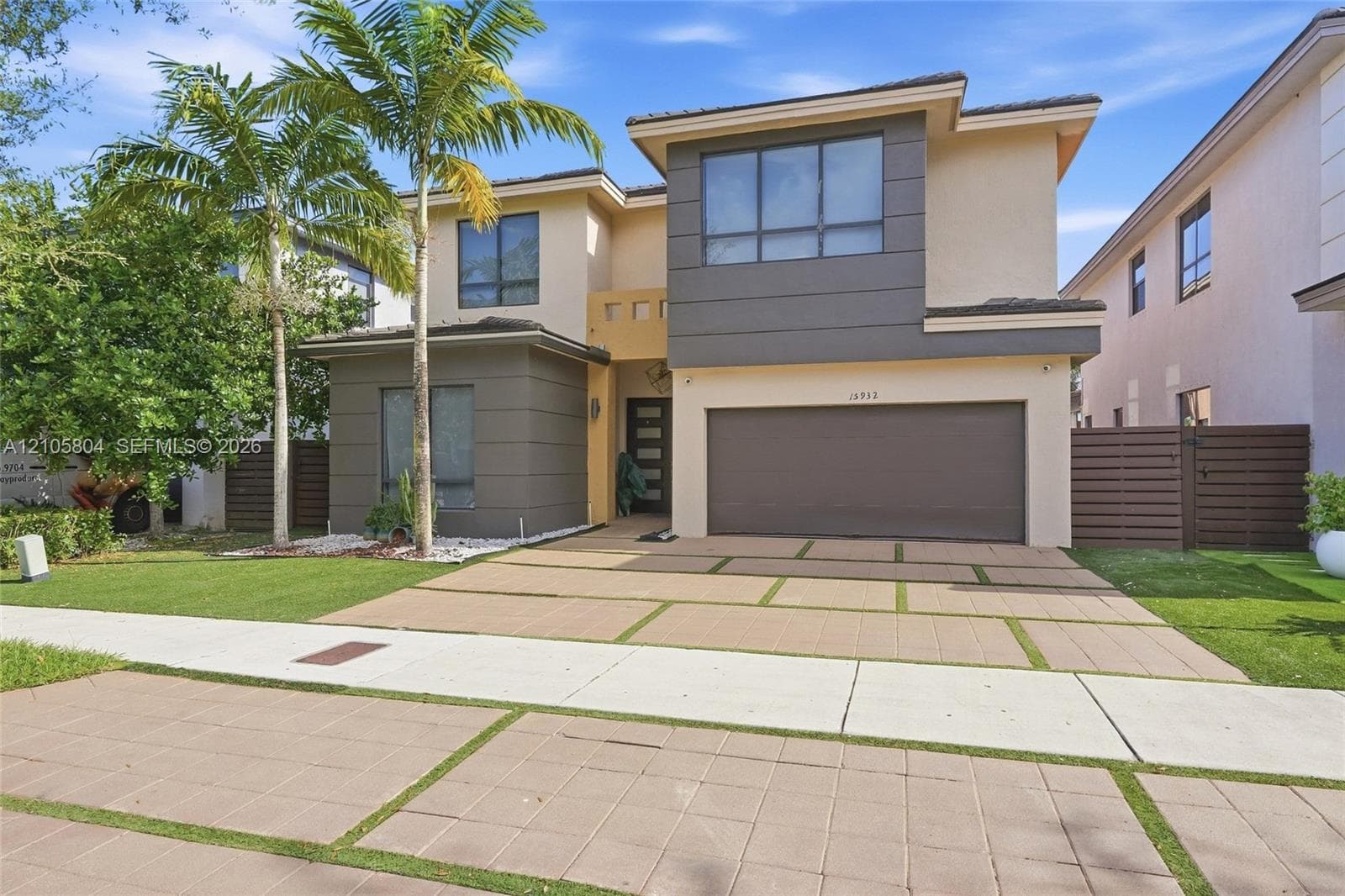 Contemporary two-story exterior featuring a multi-tone facade, large-format window groupings, two-car garage, and a geometric concrete paver driveway with integrated turf strips
