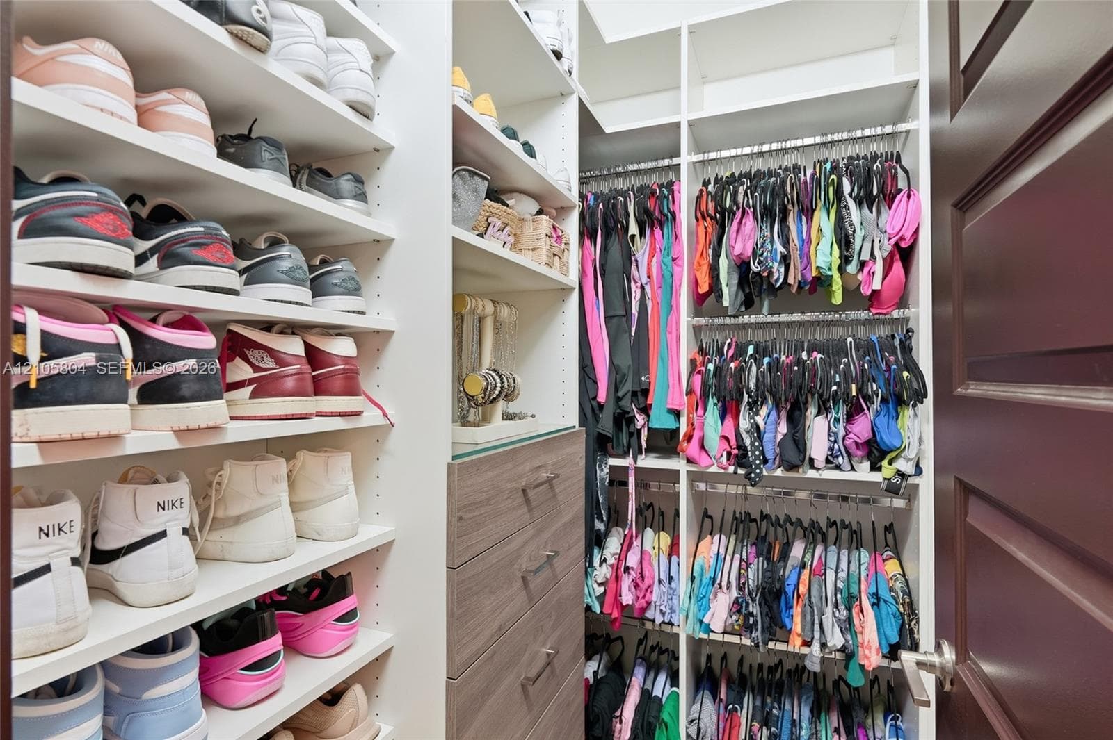 Custom walk-in closet featuring extensive built-in white shelving, integrated wood-finish cabinetry with drawers, and multi-tier hanging rods