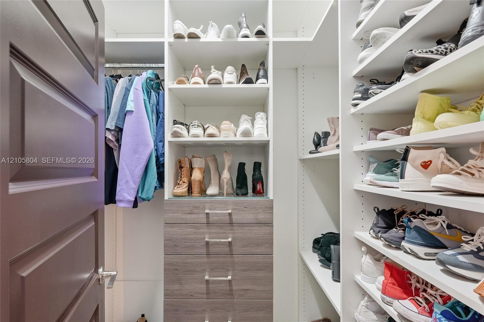 Custom walk-in closet featuring extensive built-in white shelving, integrated wood-finish cabinetry with silver-toned hardware, and a metal clothing rod