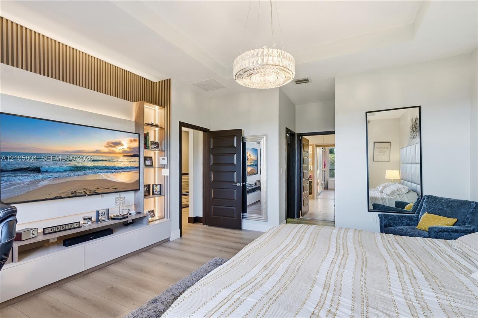 Custom built-in media center with vertical slat wood accent wall, integrated LED display shelving, recessed tray ceiling, contemporary crystal chandelier, and wood-finish flooring