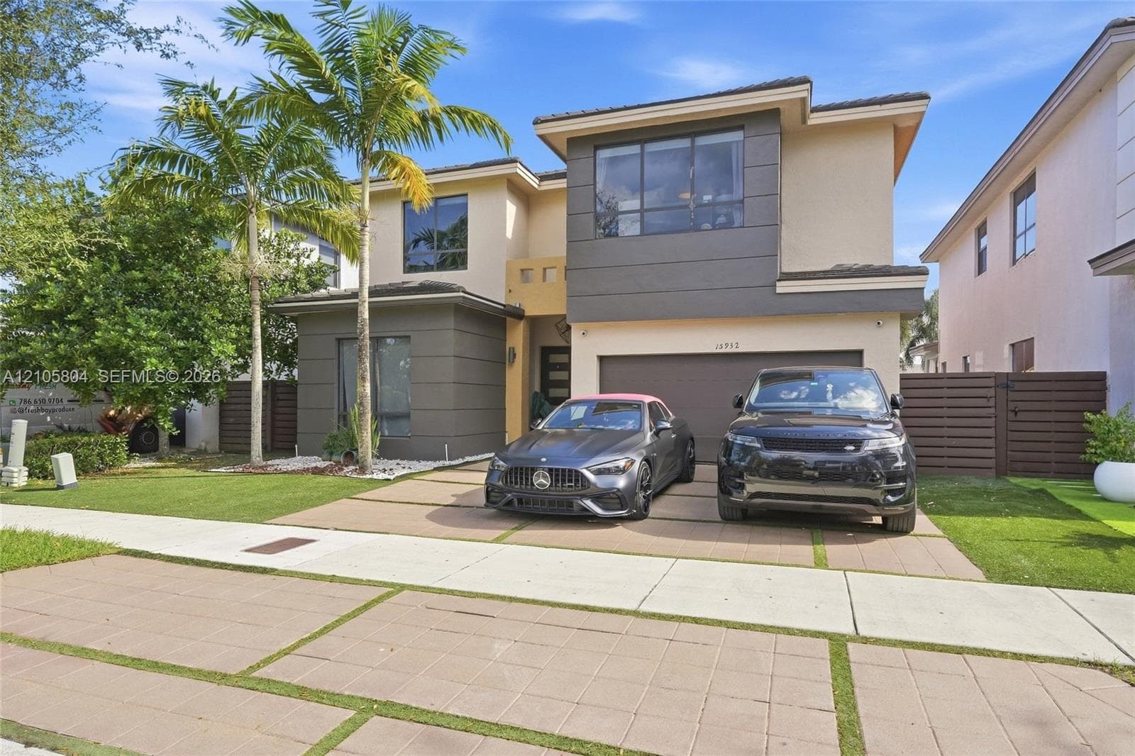 Contemporary two-story exterior featuring a multi-toned stucco facade, paver driveway with turf accents, mature palm trees, and an attached two-car garage