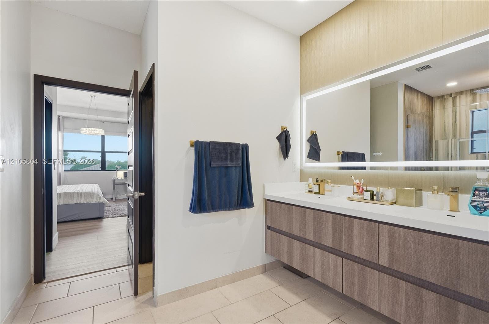 Floating vanity featuring a wood-finish cabinet, integrated double sinks, a large LED-backlit mirror, and gold-tone wall-mounted hardware