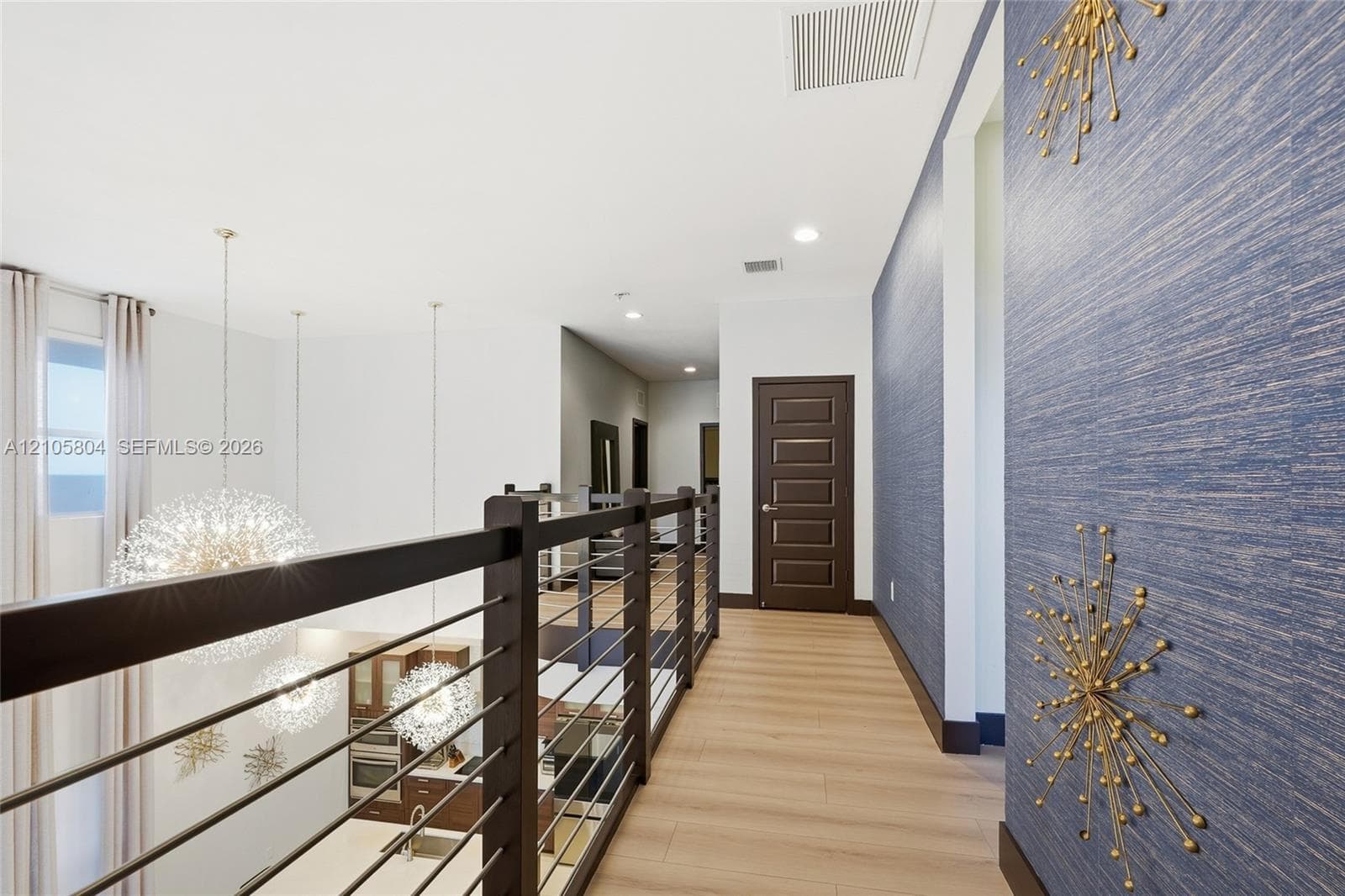 Upper-level walkway featuring wood-finish flooring, a contemporary horizontal cable railing system, textured blue wall covering, and recessed lighting
