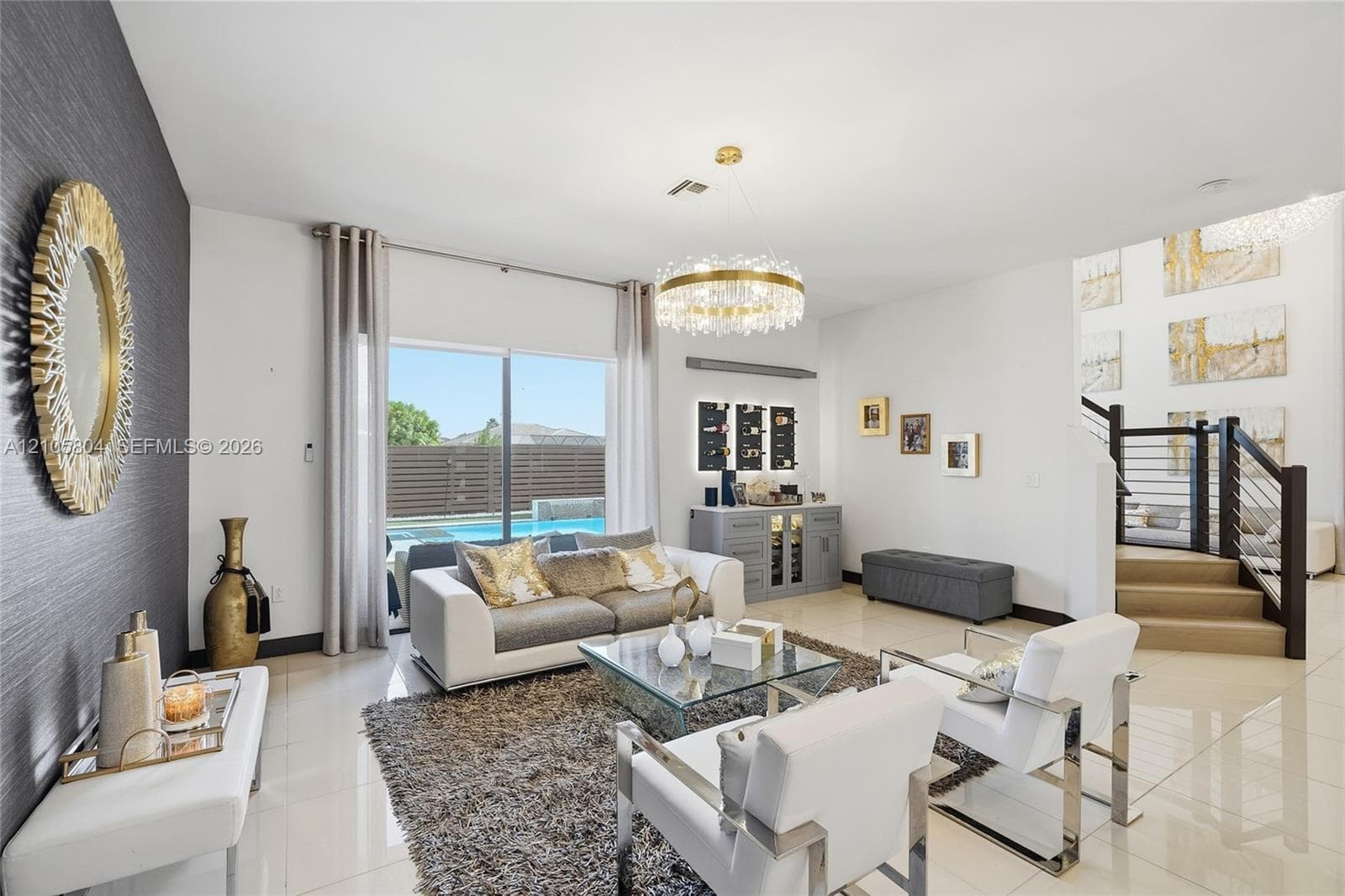 Living area featuring large-format tile flooring, a circular tiered crystal chandelier, a built-in cabinetry unit with integrated lighting, and a staircase with metal horizontal railing