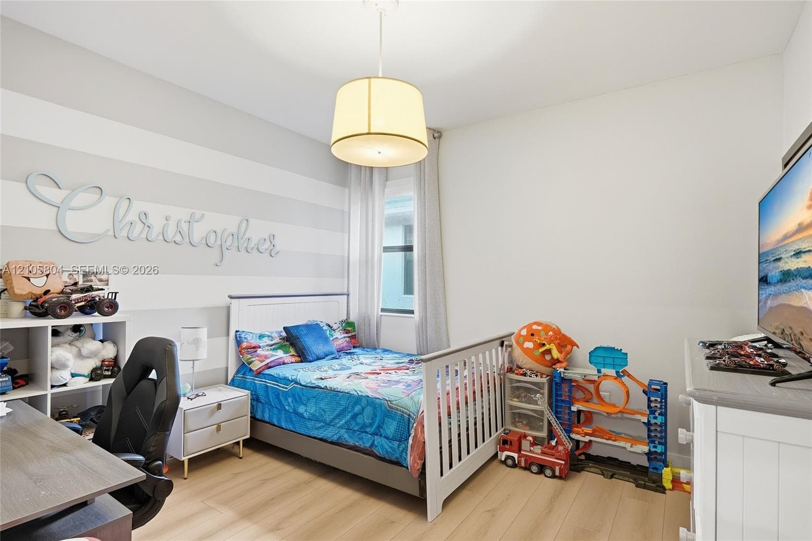 Room featuring light-toned wood-finish flooring, a drum pendant light fixture, a window with vertical blinds, and a horizontal-striped accent wall