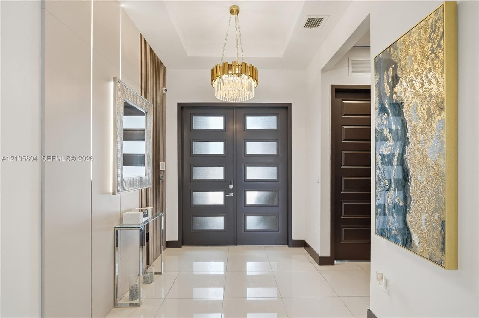 Entryway featuring a double-door entrance with frosted glass panels, tile flooring, a tiered crystal chandelier, and integrated wall paneling with recessed lighting