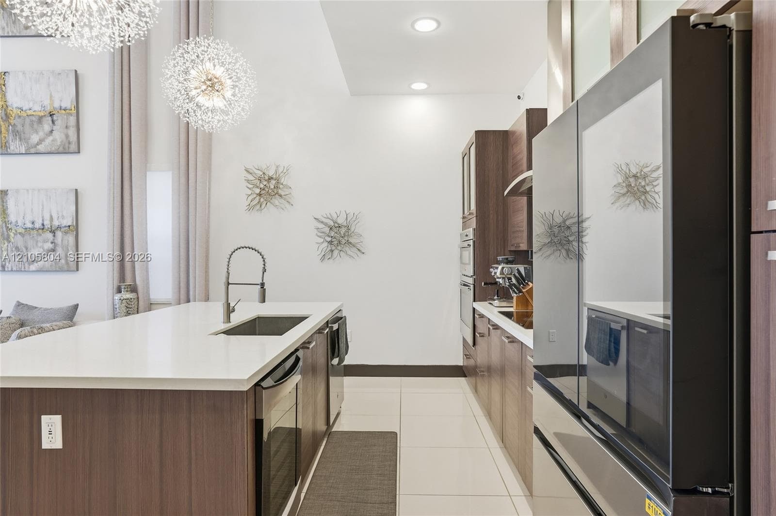 Kitchen featuring a waterfall-edge island with a quartz countertop, flat-panel cabinetry, high-ceiling drum pendant lighting, and stainless steel built-in appliances
