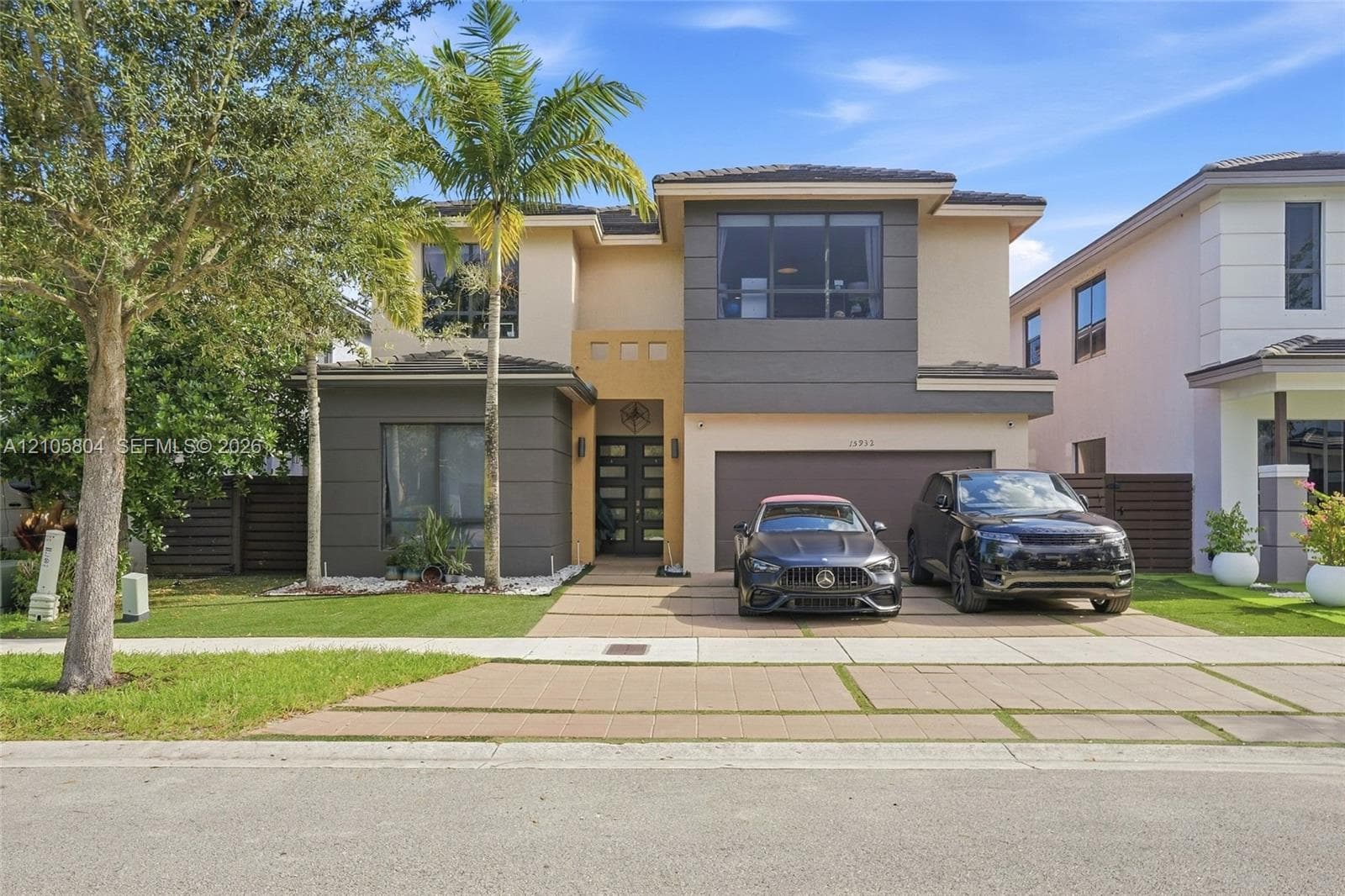 Two-story contemporary exterior featuring a concrete paver driveway, multi-toned stucco finish, large-format picture windows, and double-entry glass doors