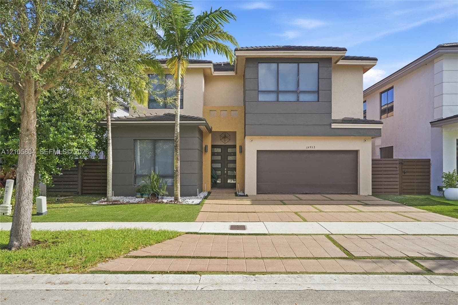 Two-story contemporary exterior featuring a multi-tonal facade, recessed entryway with multi-panel double doors, two-car garage, and geometric paver driveway