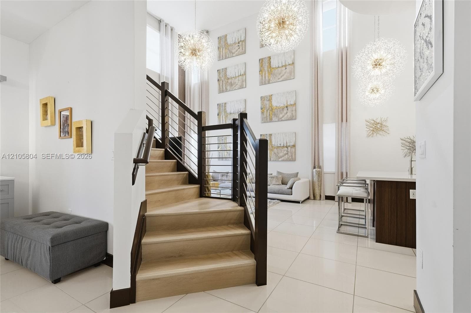 Staircase featuring wood-finish treads, dark wood posts, and a cable railing system, complemented by high-gloss floor tile and suspended globe-style pendant light fixtures