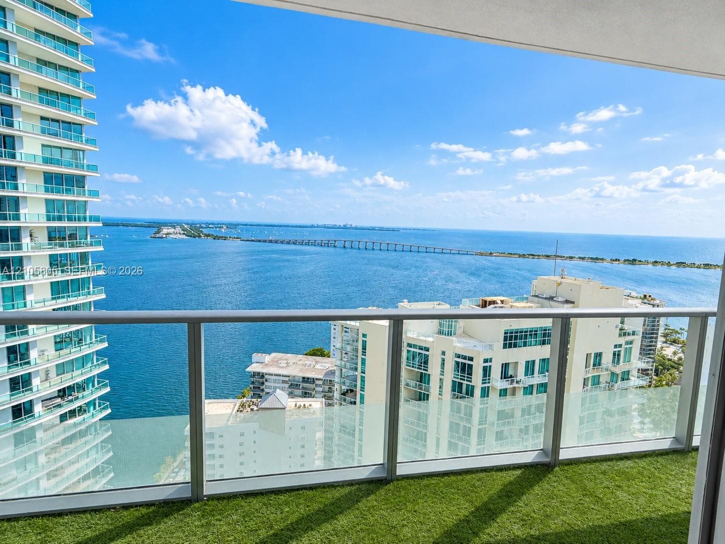 Private balcony featuring a glass-panel railing, metal frame, and artificial turf flooring