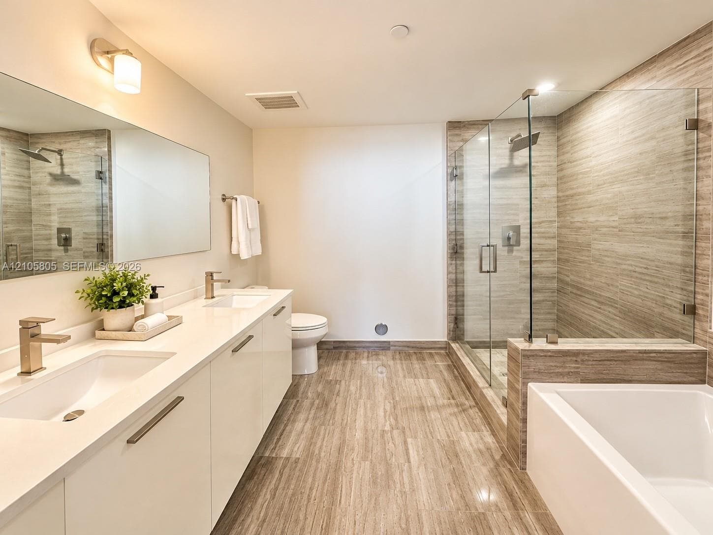 Double vanity with integrated sinks, quartz countertop, glass-enclosed walk-in shower with floor-to-ceiling textured tile, and deep soaking tub