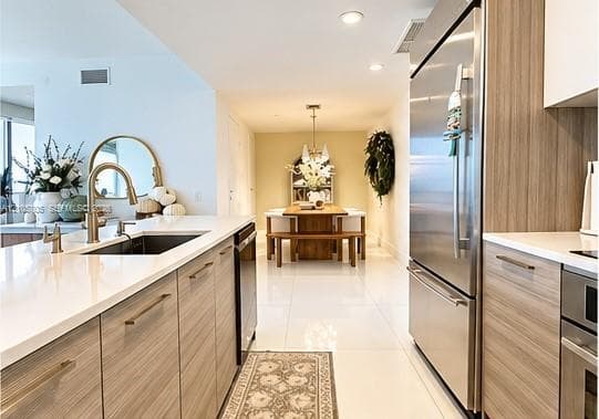 Kitchen featuring wood-finish cabinetry, white composite countertops, stainless steel appliances, and large-format tile flooring