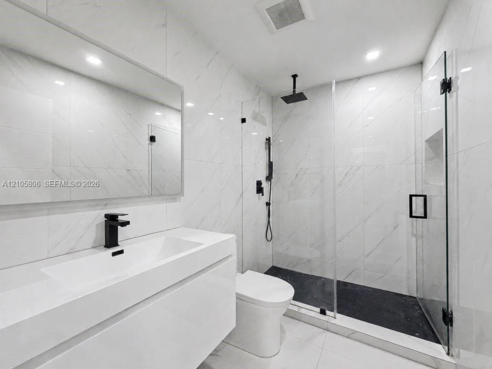 Modern bathroom featuring a wall-mounted vanity, large-format stone-look wall tile, walk-in glass shower enclosure, matte black rainfall shower system, and recessed wall niche
