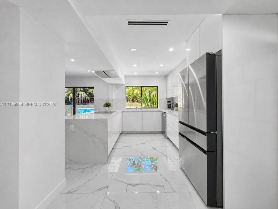 Modern kitchen featuring high-gloss cabinetry, waterfall edge stone countertops, large-format polished flooring, stainless steel appliances, and recessed lighting