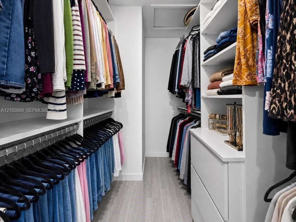 Walk-in closet featuring floor-to-ceiling white built-in shelving, custom cabinetry with integrated drawers, multi-level hanging rods, and wood-finish flooring