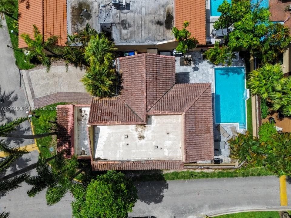 Aerial perspective of a property featuring a tile roof, an in-ground swimming pool, a stone-paved patio, and mature palm trees