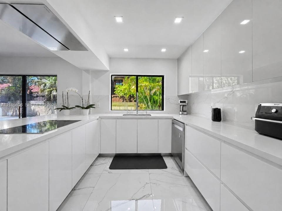 Modern kitchen featuring high-gloss cabinetry, solid surface countertops, a stainless steel range hood, stone-finish tile flooring, and integrated stainless steel appliances