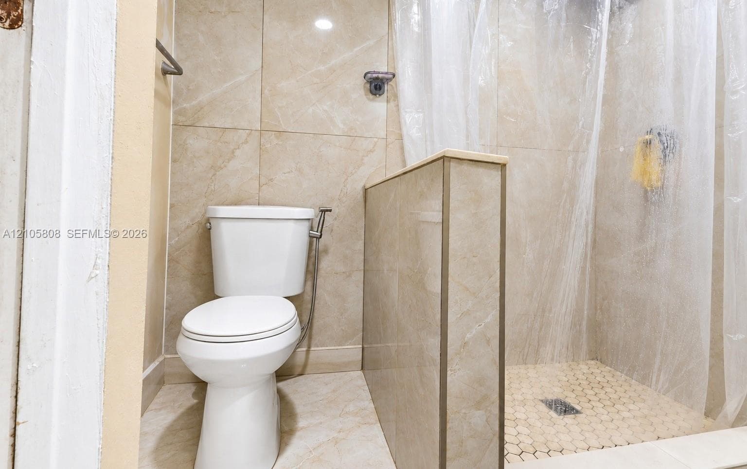 Full-height neutral stone-style wall tile, walk-in shower with stone-style hex mosaic floor tiling, and porcelain toilet