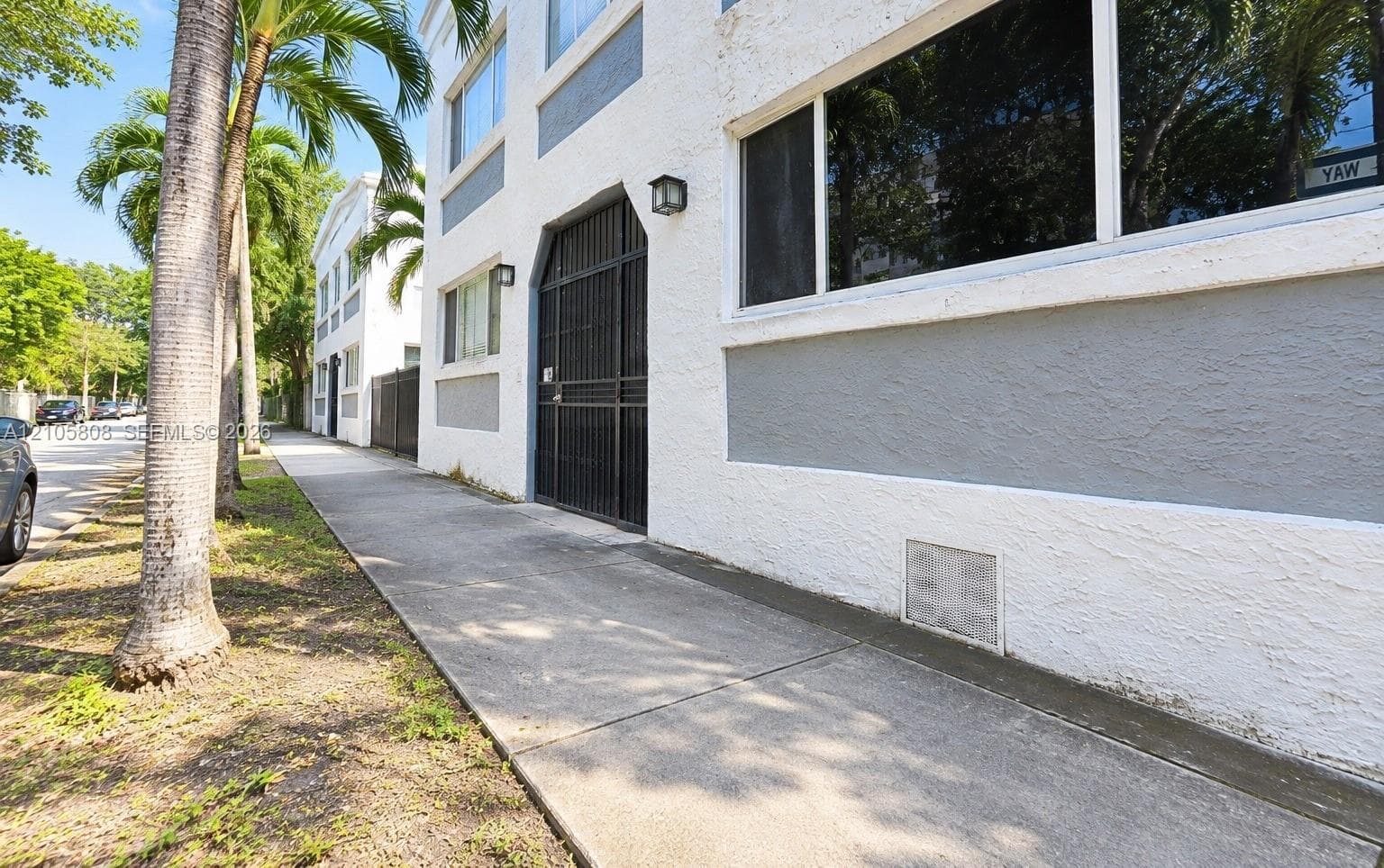 Multi-story exterior featuring textured stucco facade, contrasting grey paneling, metal security gate, and large-pane windows