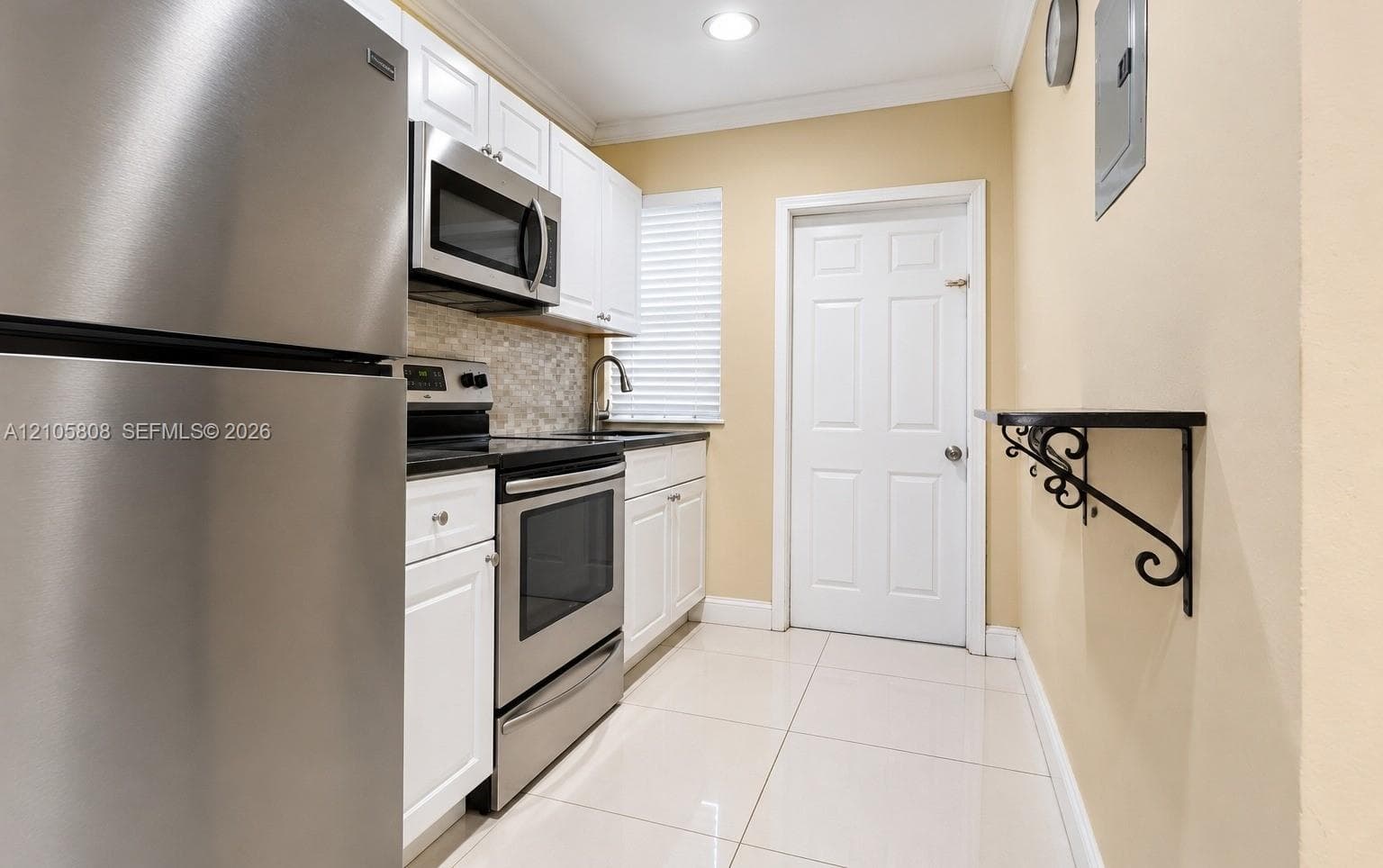 Kitchen featuring stainless steel appliances, white cabinetry, a neutral-toned backsplash, and light-colored tile flooring