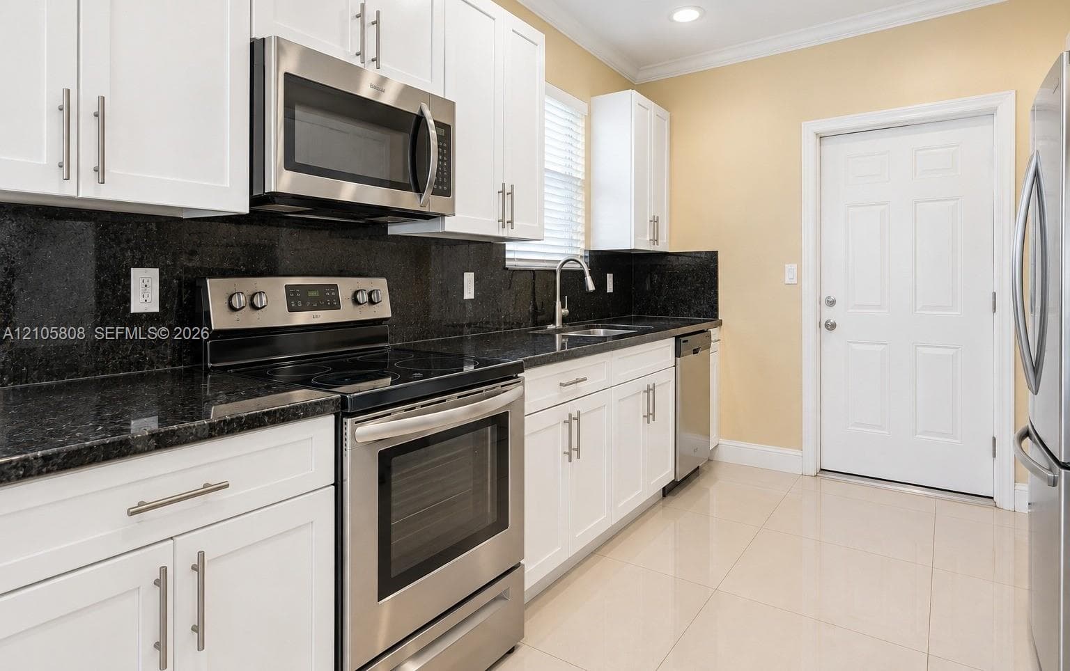 Kitchen featuring white Shaker-style cabinetry, dark stone-finish countertops, stainless steel appliances, and large-format tile flooring