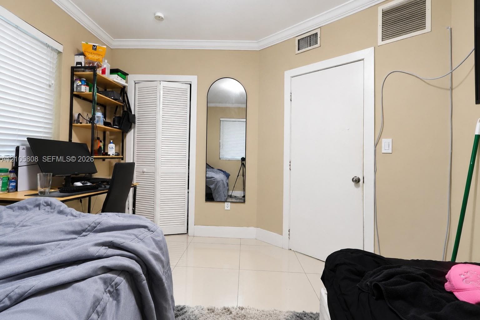 Interior space featuring large-format tile flooring, crown molding, a wall-mounted arched mirror, and white louvered bifold closet doors