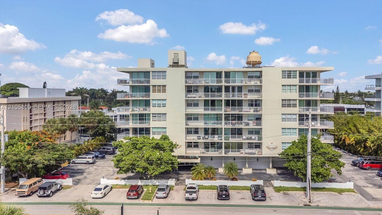 Multi-story residential building featuring reinforced concrete construction, expansive glass balcony railings, floor-to-ceiling windows, and integrated surface parking